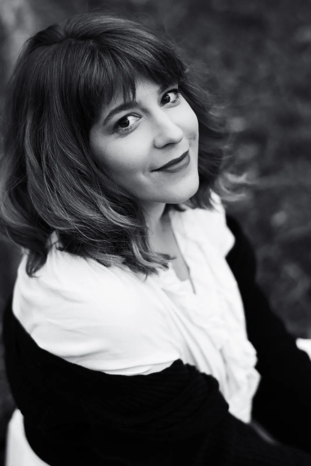 Anna Yermakova, in black and white, looking back over her shoulder at the camera, in a white ruffled blouse and a dark knitted cardigan
